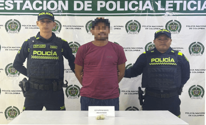 Dos polic&iacute;as y una persona civil se encuentran de pie detr&aacute;s de una mesa sobre la cual se exhiben estupefacientes incautados, con un banner institucional al fondo