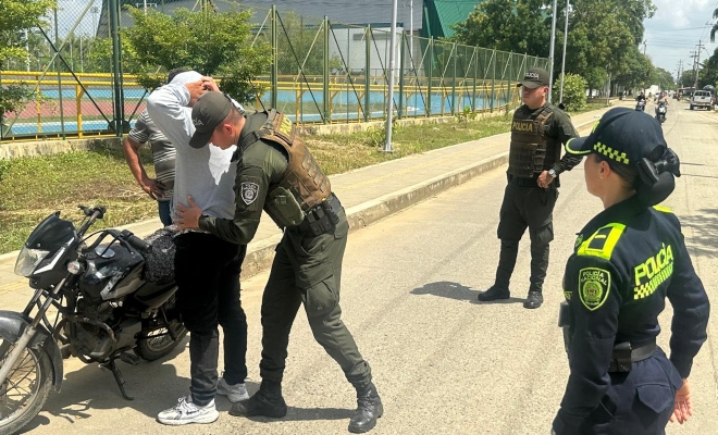 Un policía registrando a un ciudadano y dos policías prestando seguridad 