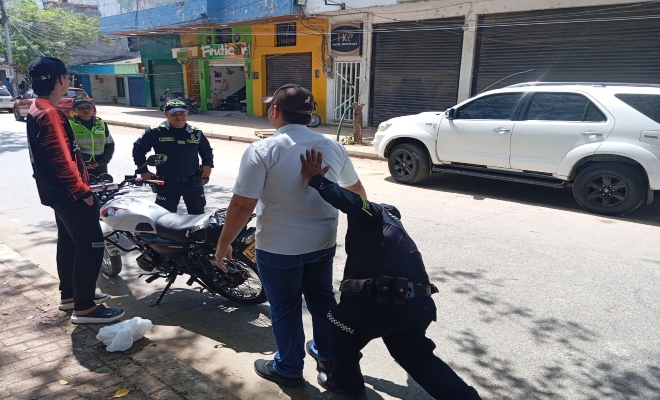 un policia realizando registro a dos ciudadano y dos policias prestando la seguridad