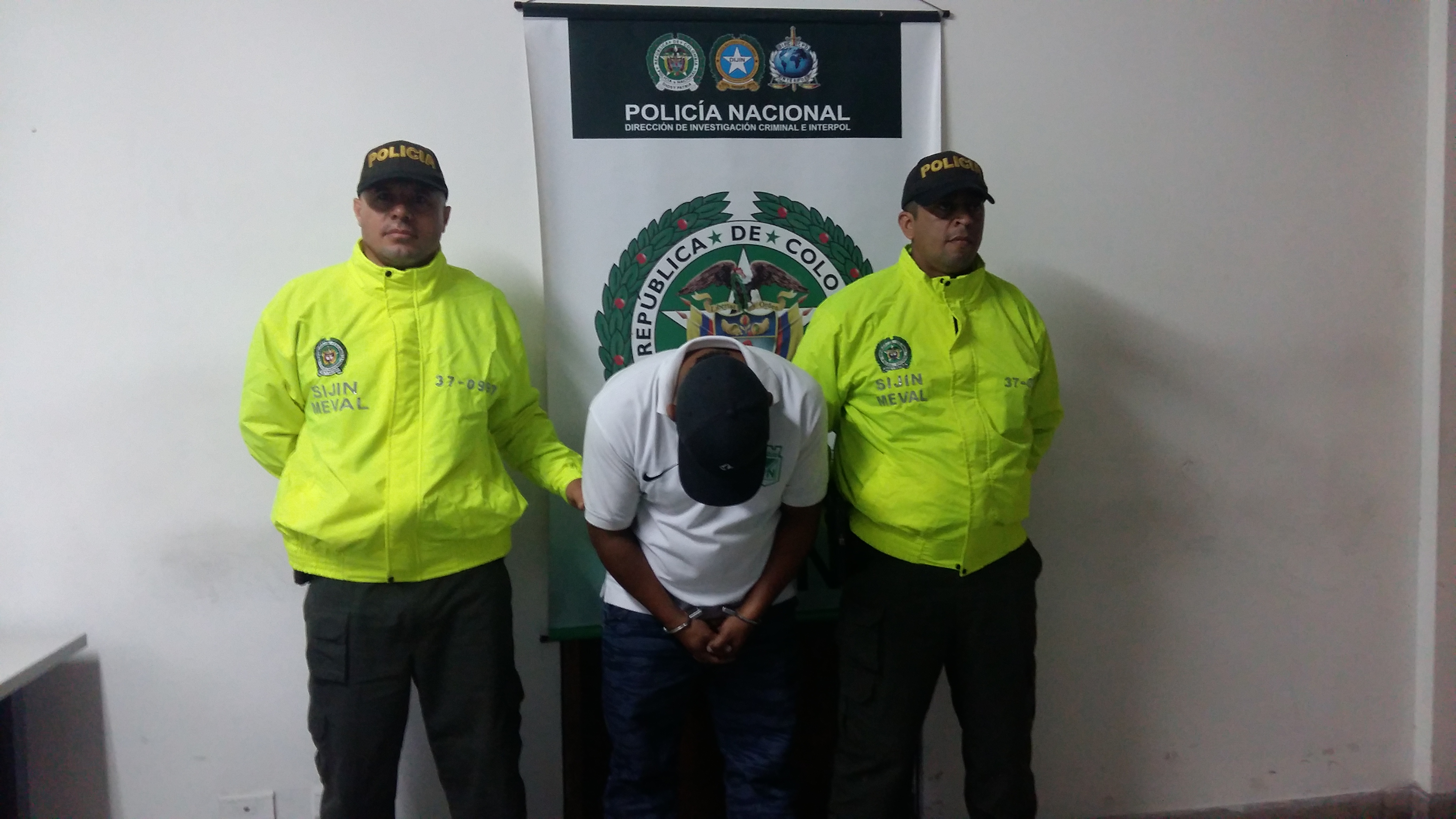 Un sujeto esposado con la cabeza agachada es custodiado por dos policías de la SIJIN en Medellín
