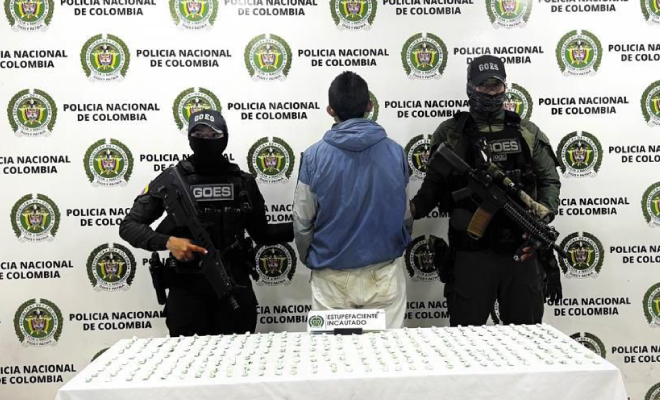 Hombre capturado en medio de dos Polic&iacute;as, en frente se encuentra ubicada una mesa con dosis de bazuco incautado