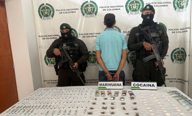 Hombre capturado en medio de dos polic&iacute;as, en frente elementos incautados