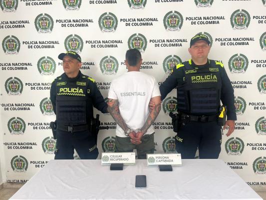 Hombre campturado de camiseta blanca en medio de dos policias
