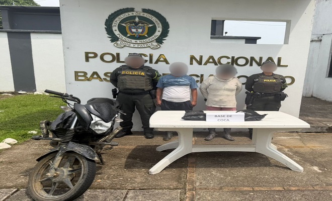 Dos polic&iacute;as junto a dos personas capturadas, en frente una mesa con estupefacientes como evidencia y una motocicleta incautada 
