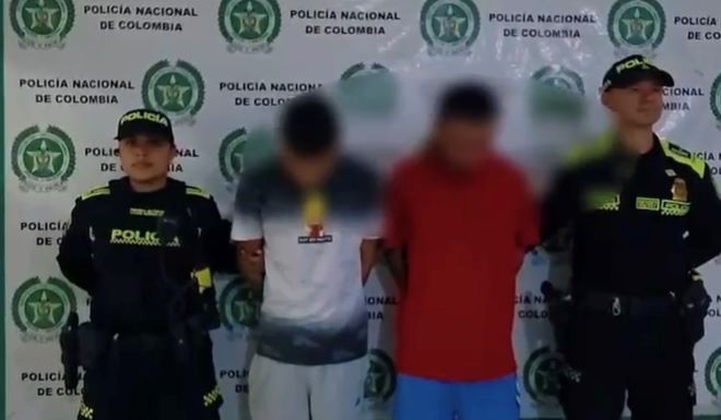 dos polic&iacute;as al lado de dos hombres capturados 