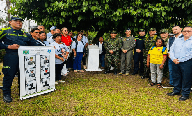 Agentes de la polic&iacute;a soldados y personal de la Fuerza A&eacute;rea junto a una cartelera varias personas con camisas de distintos colores est&aacute;n de pie frente a un muro blanco